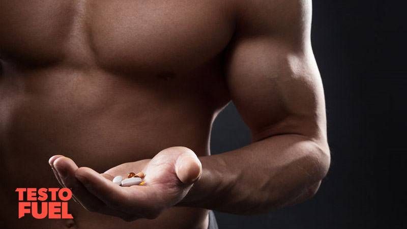 Bodybuilder with muscular arms holding a range of different pills and supplements