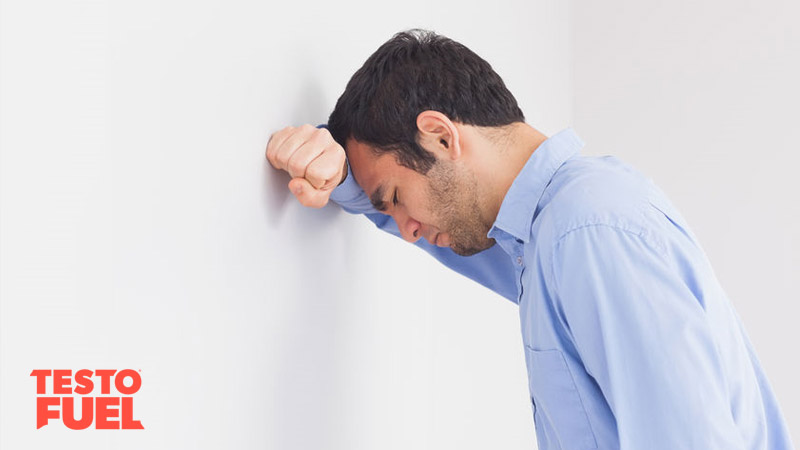 A middle-aged man leans against the wall with his head his hands