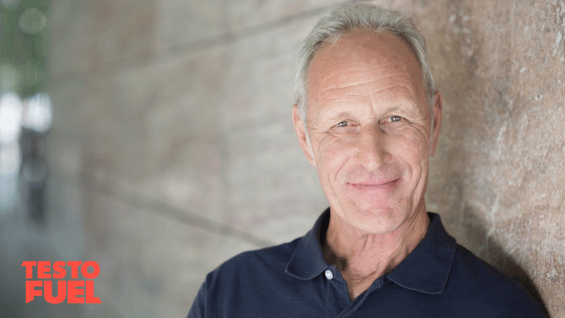 Smiling attractive grey-haired man standing alongside a receding exterior wall looking at the camera