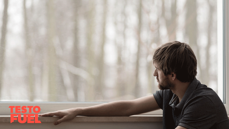 Young man looking out of a window at snow depressed