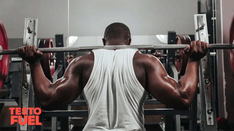 Black man in the gym barbell back squatting for hypertrophy
